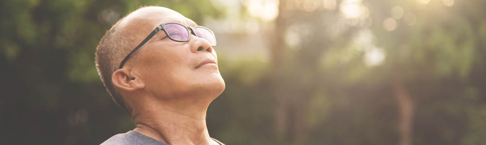 Older man leaning back so his face is point towards the sun, the background is blurred trees